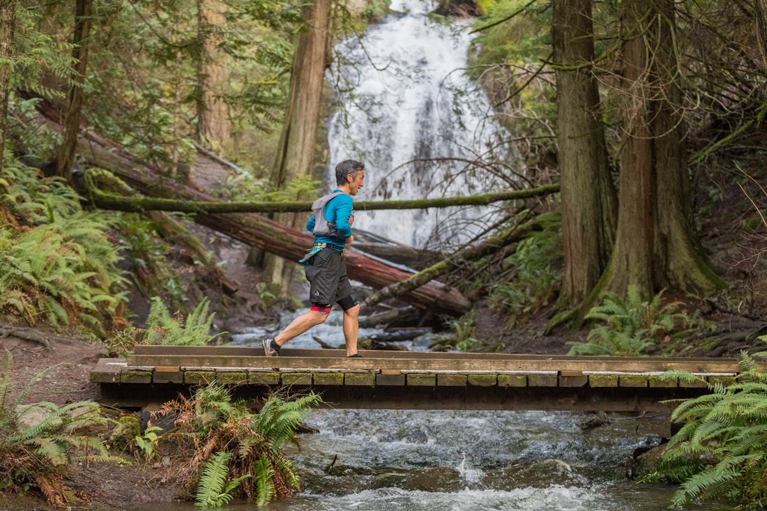 Person running across a bridge over a stream surrounded by trees.